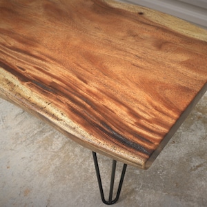 May include: A wooden coffee table with a live edge top and black hairpin legs.