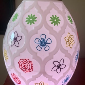 Op de afbeelding: Witte keramische diffuser met een bloemenpatroon. De diffuser heeft een geometrisch ontwerp met bloemen in verschillende kleuren, waaronder rood, blauw, groen en geel.