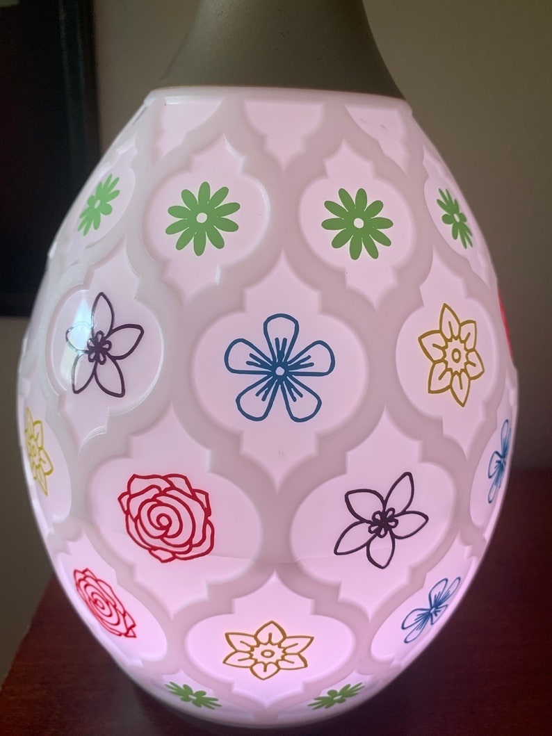 Op de afbeelding: Witte keramische diffuser met een bloemenpatroon. De diffuser heeft een geometrisch ontwerp met bloemen in verschillende kleuren, waaronder rood, blauw, groen en geel.