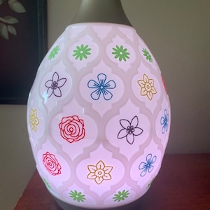 May include: White ceramic essential oil diffuser with a floral pattern. The diffuser has a gray top and a light pink glow.