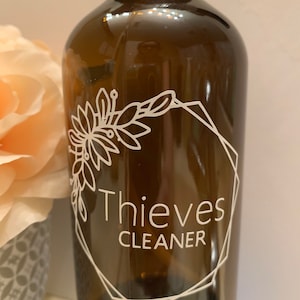 May include: A brown glass spray bottle with a white label that says "Thieves Cleaner" in a geometric frame with a floral design.