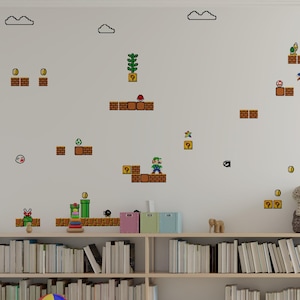 Könnte beinhalten: Eine weiße Wand, verziert mit Wandaufklebern im Super Mario Bros.-Stil. Die Szene zeigt pixelige Charaktere, Blöcke und Wolken, die eine verspielte, von Videospielen inspirierte Ästhetik schaffen. Ein Bücherregal mit Büchern, ein Schaukelpferd und ein Ball befinden sich im Vordergrund.