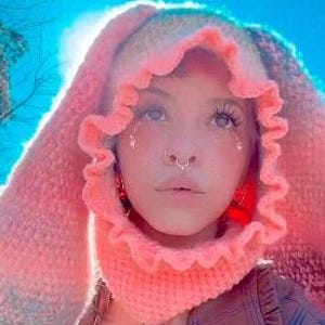 Może przedstawiać: Osoba w różowo-białym dzianym kapturze z falbanką. Kaptur ma uszy królicze, a osoba ma kolczyk w nosie.