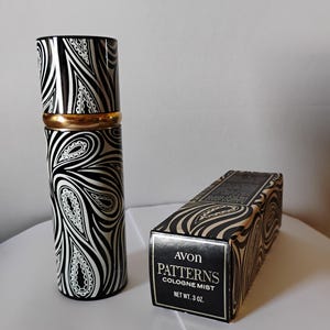 May include: A cylindrical Avon Patterns cologne mist bottle with a black and white paisley pattern and a gold band, accompanied by its matching rectangular cardboard box featuring the text Avon Patterns Cologne Mist Net Wt. 3 oz.