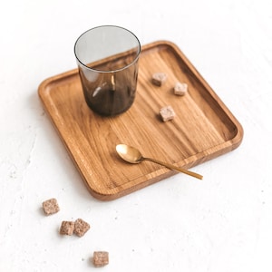 Puede incluir: Una bandeja de madera con un vaso, una cuchara de oro y cubos de azúcar moreno. La bandeja está sobre una superficie blanca.