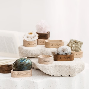May include: A collection of various crystals and stones displayed on wooden stands. The stands are engraved with the text "Amor Crystal". The crystals are displayed on a light gray textured surface.