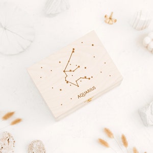 The picture shows top of the natural wooden box which features an engraving of Aquarius constellation sign with small stars and the word Aquarius in capital letters. The start sign can be selected in personalization part.