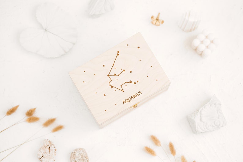 The picture shows top of the natural wooden box which features an engraving of Aquarius constellation sign with small stars and the word Aquarius in capital letters. The start sign can be selected in personalization part.