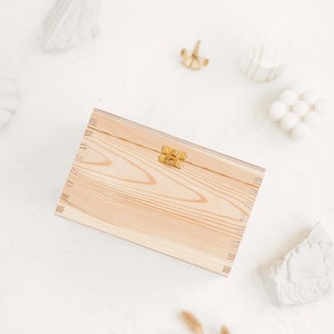 The picture shows a side of the natural wooden box which contains the metal clasp. The box is positioned in a white background with white decorations.