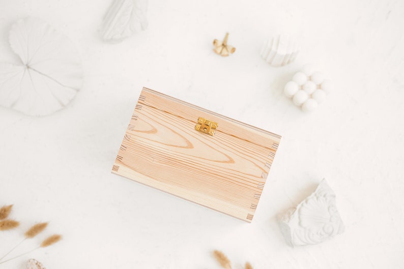 The picture shows a side of the natural wooden box which contains the metal clasp. The box is positioned in a white background with white decorations.
