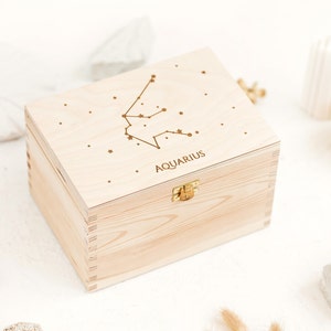 Box made out of natural wood shown sideways. The top of the box has an engraving of the Aquarius constellation sign and small stars. Wooden box comes with a metal clasp.