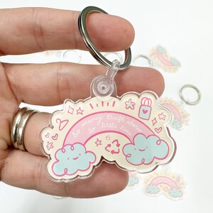 May include: A pink and white rainbow keychain with the text "so many thrift stores so little time". The keychain features two clouds with smiley faces and a recycling symbol.