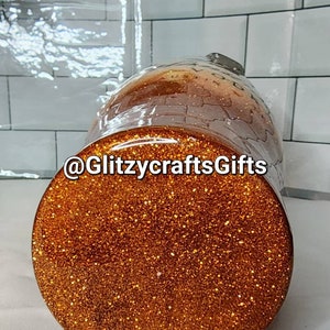May include: A gold glitter tumbler with the text "@GlitzycraftsGifts" on the side. The tumbler is sitting on a white tiled surface.