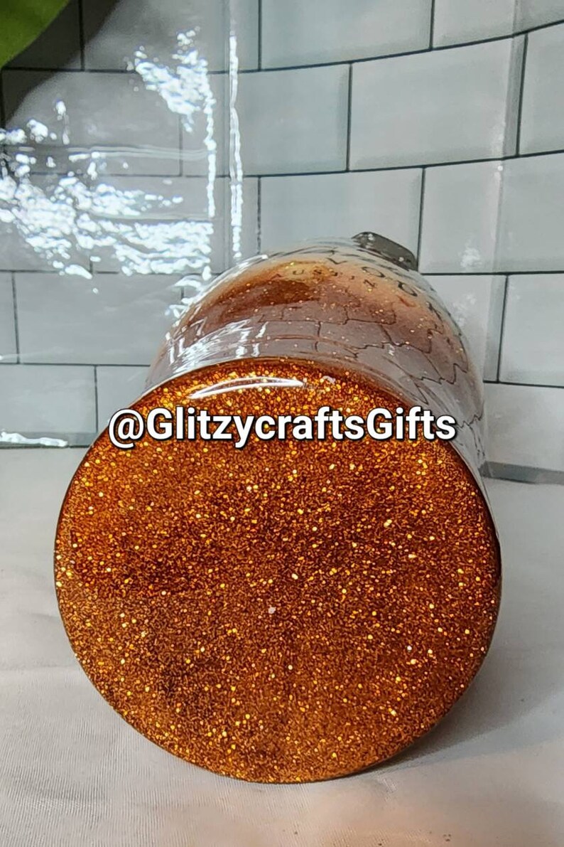 May include: A gold glitter tumbler with the text "@GlitzycraftsGifts" on the side. The tumbler is sitting on a white tiled surface.