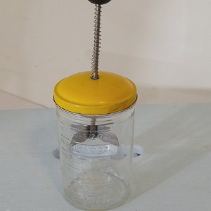 May include: A yellow and clear glass food mill with a black knob on top. The mill has markings for measuring ounces and cups.