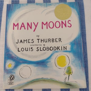 May include: A vintage children's book cover with a blue, yellow, and white illustration of a night sky with multiple moons. The title of the book is "MANY MOONS" by JAMES THURBER, illustrated by LOUIS SLOBODKIN.