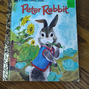 May include: Vintage "Peter Rabbit" Little Golden Book. The cover features an illustration of Peter Rabbit wearing a blue vest, holding a green vegetable, and standing in a garden with sunflowers. The title is in red letters against a blue sky.