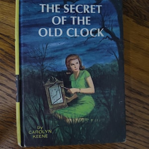 May include: A vintage book cover for "The Secret of the Old Clock" by Carolyn Keene. The cover features a woman in a green dress holding a clock, set against a dark blue night scene with trees and grass. The title is in large white letters.