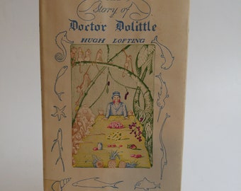 May include: The cover of a vintage book titled "The Story of Doctor Dolittle" by Hugh Lofting. The cover features a colorful illustration of a man in a blue shirt and a green hat sitting at a table with monkeys and other animals around him.