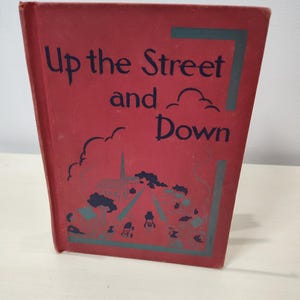 May include: A vintage book titled "Up the Street and Down" with a red cover. The title is in dark blue script. The cover features a teal illustration of a street scene with trees and buildings. The book is standing upright.
