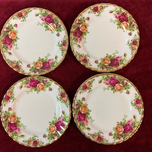 May include: Set of four white ceramic dessert plates with a gold rim and a floral pattern featuring red, yellow, and pink roses.
