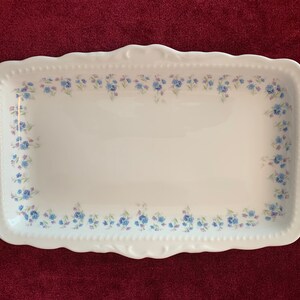 May include: A white rectangular serving platter with a floral border of blue and purple flowers. It has gold-coloured handles and trim. The edges are scalloped.