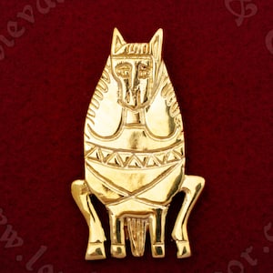 May include: A gold-coloured metal brooch depicting a stylised horse. The horse is sitting with its legs folded and has a detailed design on its body.