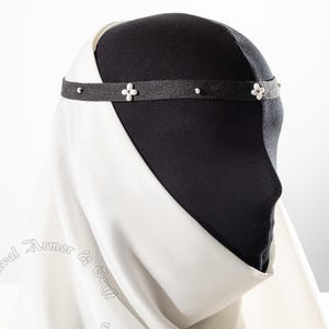 May include: A black headband with small white floral and pearl accents. The headband is worn on a black head form and is paired with a white fabric draped around the form. The text "Medieval Armor & Craft" and website address are visible.