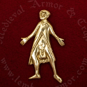 May include: A gold-colored metal pendant depicting a person in a long robe with their arms outstretched. The pendant is on a red background.