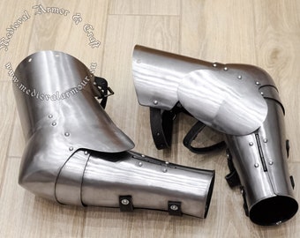 May include: A pair of silver metal elbow guards with leather straps. The guards are made of metal plates and have a rounded shape. The straps are attached to the guards with rivets. The guards are designed to protect the elbows from injury.
