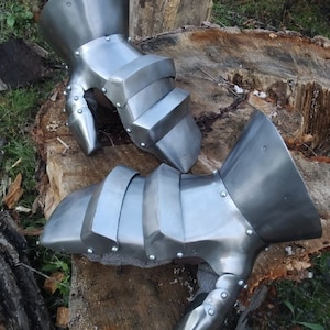 K&ouml;nnte beinhalten: Ein Paar silberne Metallhandschuhe mit einem segmentierten Design. Die Handschuhe haben ein spitzes Fingerdesign und bestehen aus Metallplatten.