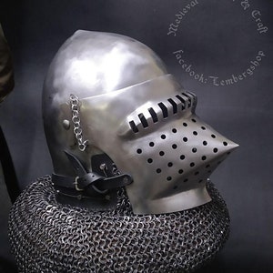 May include: A silver helmet with a visor and a chainmail coif. The helmet has a pointed top and a beak-like visor. The chainmail coif is made of small metal rings.