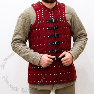 May include: A red padded leather vest with silver rivets and black leather straps. The vest has a V-neck and is fastened with buckles.