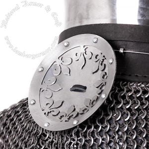 Könnte beinhalten: Eine silberfarbene, ovale Metallplatte mit floralem Design, die an einem schwarzen Lederriemen befestigt ist. Die Platte ist an einem Kettenhemd befestigt, mit dem Text "Medieval Armor & Craft" sichtbar.