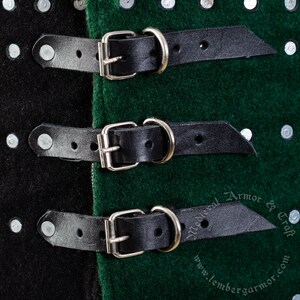 May include: Close-up of three black leather straps with silver buckles, attached to a green and black fabric surface. The straps are secured with metal rings.