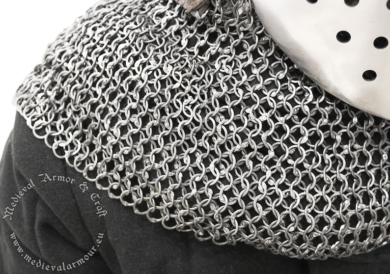 May include: A silver chainmail collar, a type of medieval armor, made of interlocking metal rings. The collar is shown on a dark fabric background.