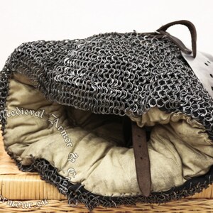 May include: A medieval chainmail coif with a leather strap and a padded lining. The coif is made of interlocking metal rings and is designed to protect the head and neck.