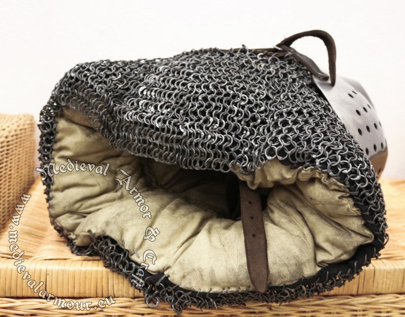 May include: A medieval chainmail coif with a leather strap and a padded lining. The coif is made of interlocking metal rings and is designed to protect the head and neck.