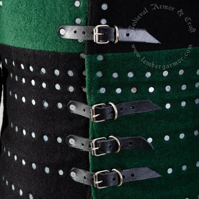May include: Close-up of a black and green garment with silver studs and four black leather straps with silver buckles. The straps are fastened to the garment with stitching. The text "Medieval Armor & Craft" and "www.lembergarmor.com" is visible on the garment.