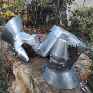 K&ouml;nnte beinhalten: Ein Paar mittelalterliche Handschuhe aus Metall mit silberner Oberfl&auml;che. Die Handschuhe sind so konzipiert, dass sie die H&auml;nde und Finger im Kampf sch&uuml;tzen. Die Handschuhe bestehen aus mehreren Metallplatten, die miteinander vernietet sind. Die Handschuhe haben eine spitze Form an den Kn&ouml;cheln und eine abgerundete Form auf der R&uuml;ckseite der Hand.