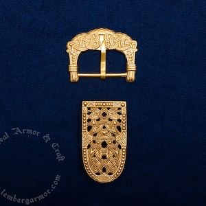 Op de afbeelding: Twee goudkleurige metalen riemgespen met ingewikkelde Keltische knoopontwerpen. De gesp aan de linkerkant is een standaardgesp met een tong en lus. De gesp aan de rechterkant is een decoratieve gesp met een rechthoekige vorm.