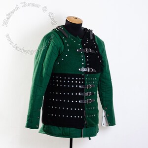 May include: A black and green padded armor vest with leather straps and buckles. The vest has metal rivets throughout.