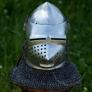May include: A silver helmet with a face mask and a chainmail collar. The helmet has a pointed top and a visor with a small opening for the eyes. The face mask has a series of small holes for ventilation. The chainmail collar is made of interlocking metal rings.