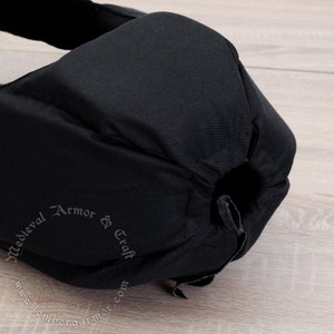 May include: Black padded helmet with a drawstring closure. The helmet is made of fabric and has the text "Medieval Armor & Craft www.lembergarmor.com" printed on the side.