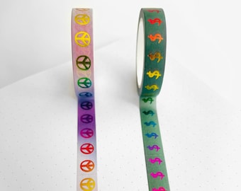 May include: Two rolls of decorative washi tape. One roll features a gradient of colours with peace symbols. The other roll is green with colourful dollar signs. Both rolls are on a white surface.