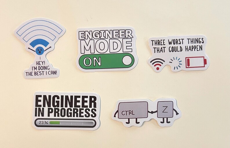 Peut inclure: Cinq autocollants en vinyle sur le th&egrave;me de l'ing&eacute;nierie. L'un montre un symbole Wi-Fi avec le texte "HEY! I'M DOING THE BEST I CAN!", un autre "ENGINEER MODE ON", un troisi&egrave;me "THREE WORST THINGS THAT COULD HAPPEN" avec des ic&ocirc;nes, "ENGINEER IN PROGRESS" avec une barre de chargement &agrave; 23%, et une paire de touches "CTRL Z".