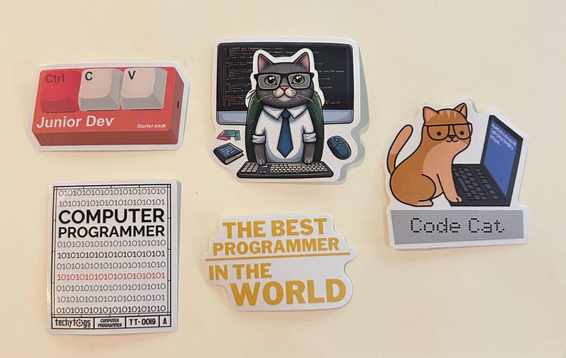 Peut inclure: Un ensemble de cinq autocollants en vinyle sur le th&egrave;me de la programmation. Les motifs incluent des touches de clavier rouges marqu&eacute;es Junior Dev, un chat &agrave; lunettes devant un ordinateur, un code binaire avec le texte COMPUTER PROGRAMMER, un autocollant jaune indiquant THE BEST PROGRAMMER IN THE WORLD, et un chat orange avec un ordinateur portable marqu&eacute; Code Cat.