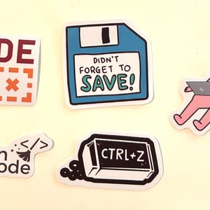 Peut inclure: Un ensemble de cinq autocollants en vinyle avec des motifs technologiques : une &eacute;tiquette rouge CODE, une disquette bleue avec le texte DIDN'T FORGET TO SAVE!, un personnage rose utilisant un ordinateur portable, une &eacute;tiquette clean code et une gomme noire CTRL+Z.