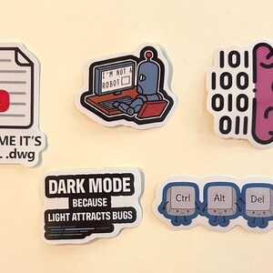 Peut inclure: Cinq autocollants en vinyle avec des motifs technologiques : une ic&ocirc;ne de document avec le texte 'TRUS ME IT'S FINAL .dwg', un robot devant un ordinateur avec 'I'M NOT A ROBOT', un cerveau avec du code binaire, 'DARK MODE BECAUSE LIGHT ATTRACTS BUGS' et les touches Ctrl Alt Del.