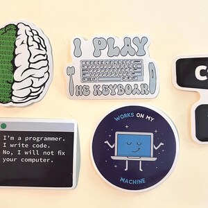 Peut inclure: Un ensemble de cinq autocollants en vinyle avec des motifs informatiques : un cerveau binaire, un clavier avec le texte I PLAY THE KEYBOARD, un graphique de touche Ctrl+V, une fen&ecirc;tre avec du texte sur la r&eacute;paration d'ordinateurs et un portable.